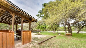 Un área de picnic techada con bancos y mesas, rodeada de árboles.