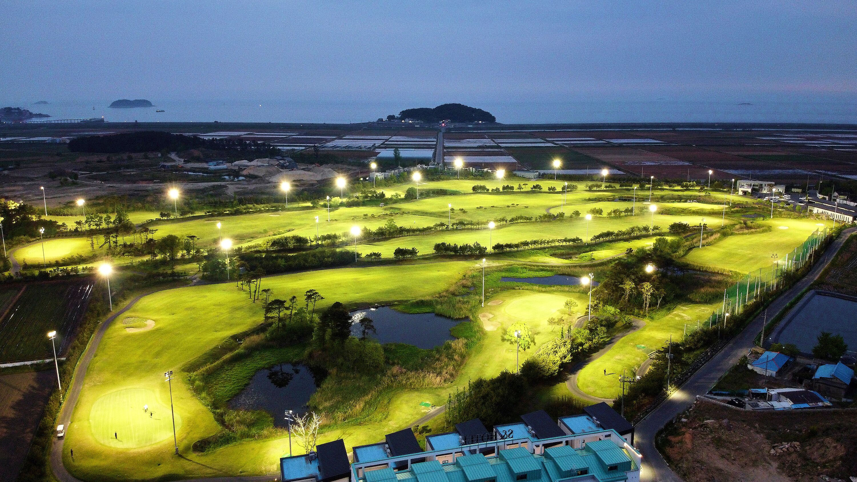 An aerial view of a golf course at night with illuminated paths and ponds.