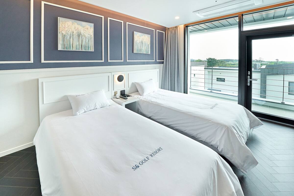 Habitación de hotel con dos camas, un ventanal grande y obras de arte en la pared.