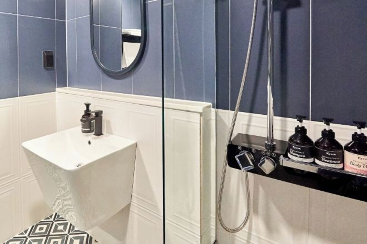 A bathroom with a white sink, a mirror, and a shower area with bottles of shampoo and conditioner.