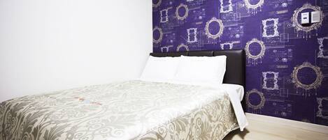 A neatly made bed with a patterned bedspread, a dark headboard, and a purple wallpaper with ornate designs.