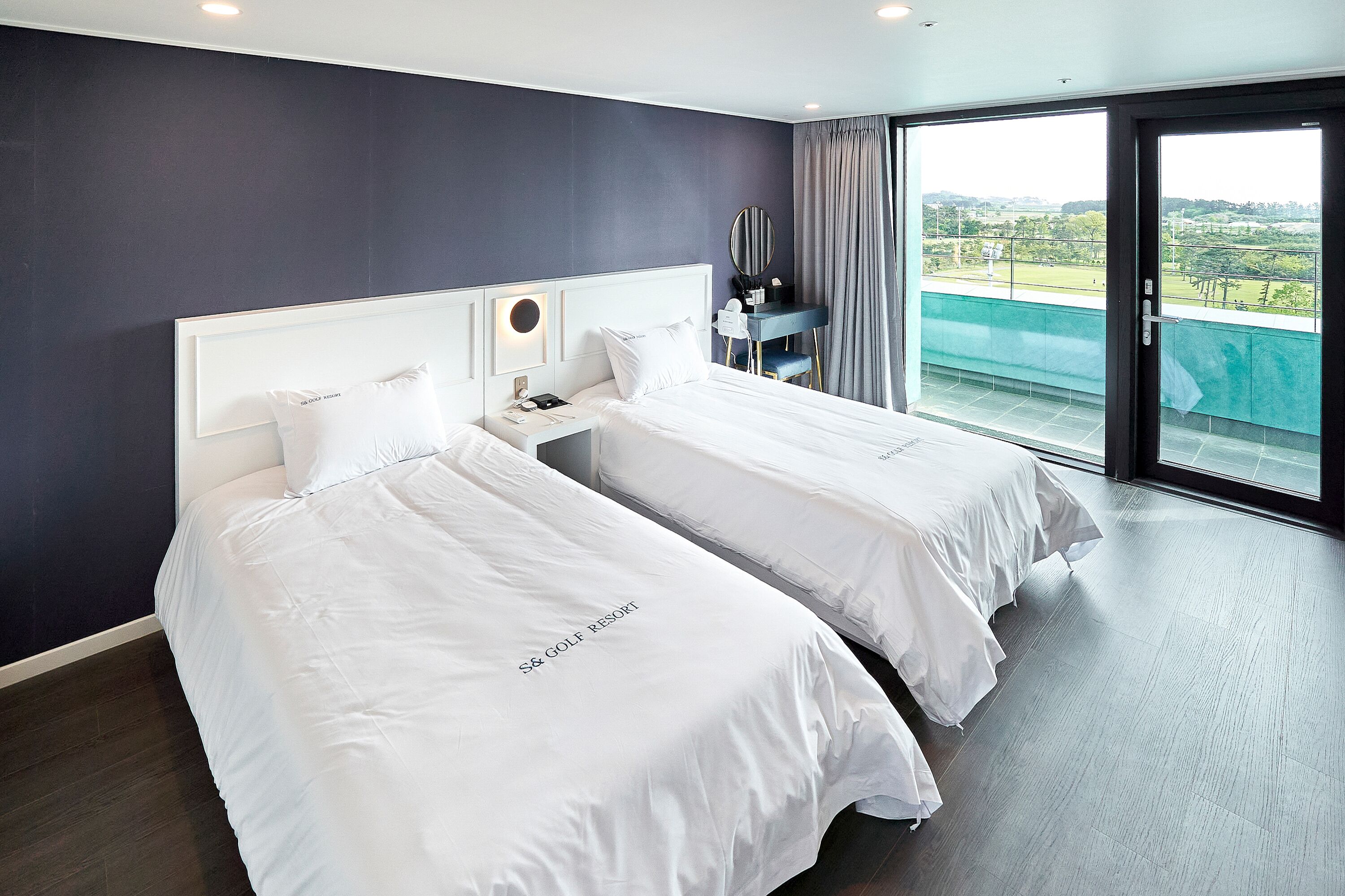 A hotel room with two beds, a desk, and a large window with a view.