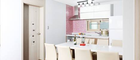 Una cocina moderna con armarios blancos, un salpicadero rosa y una zona de comedor con mesa y sillas blancas.