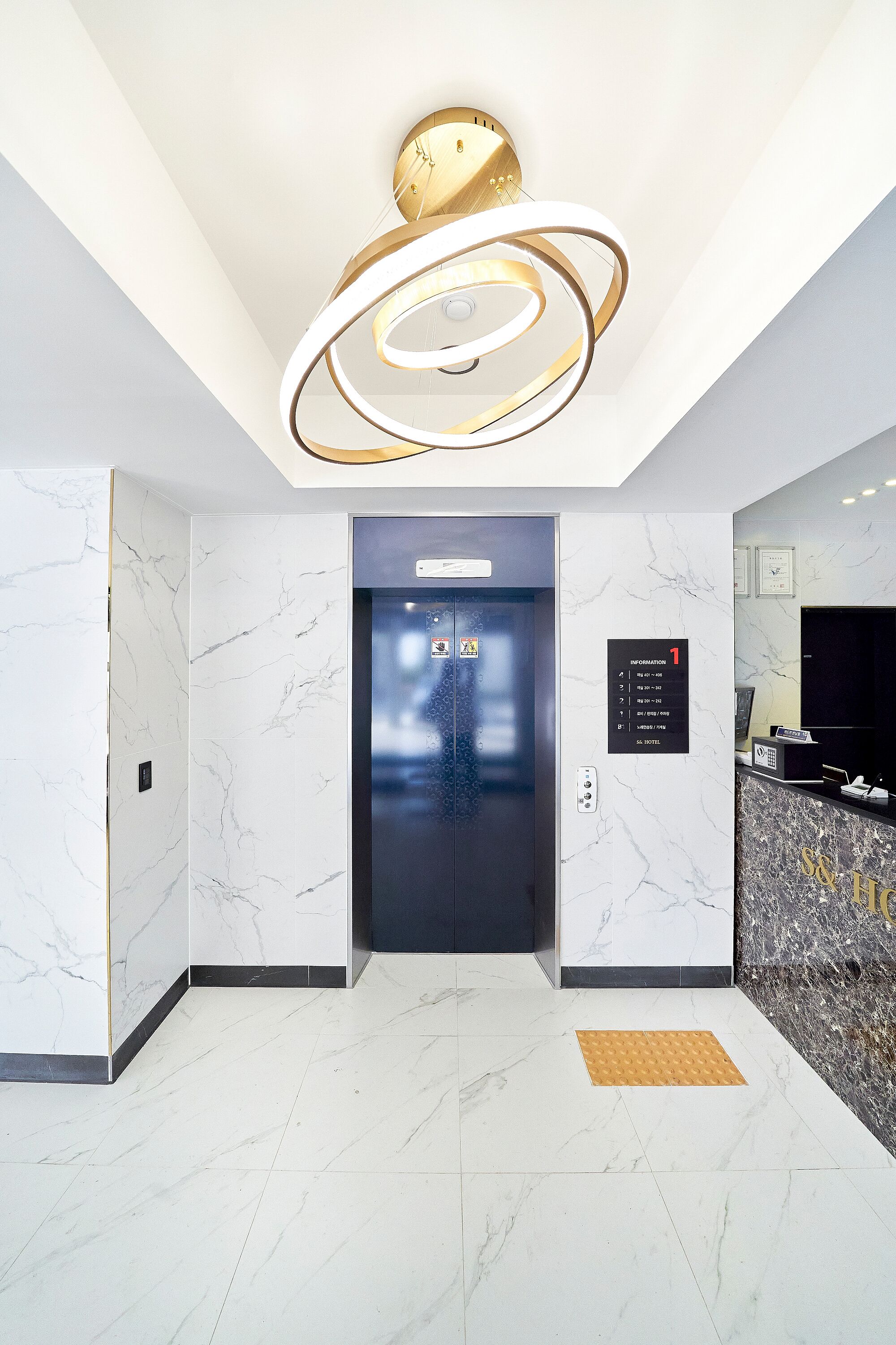 A modern elevator with a digital display, a marble wall, and a reception desk with a gold and black design.