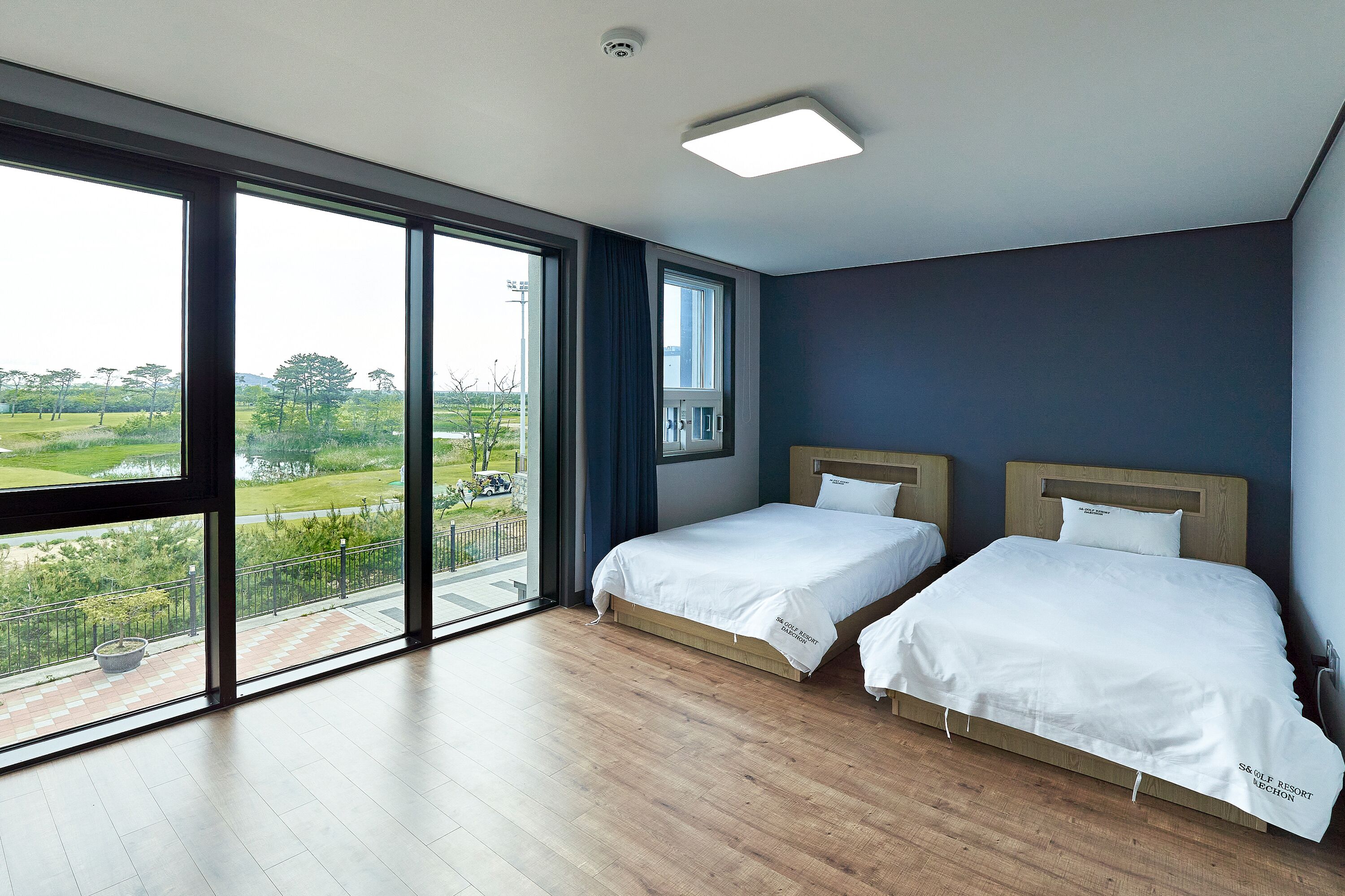 A hotel room with two beds, large windows, and a view of a green landscape.