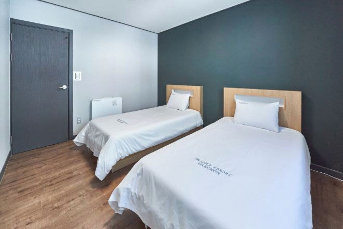 A hotel room with two single beds, a wooden floor, and a dark wall.