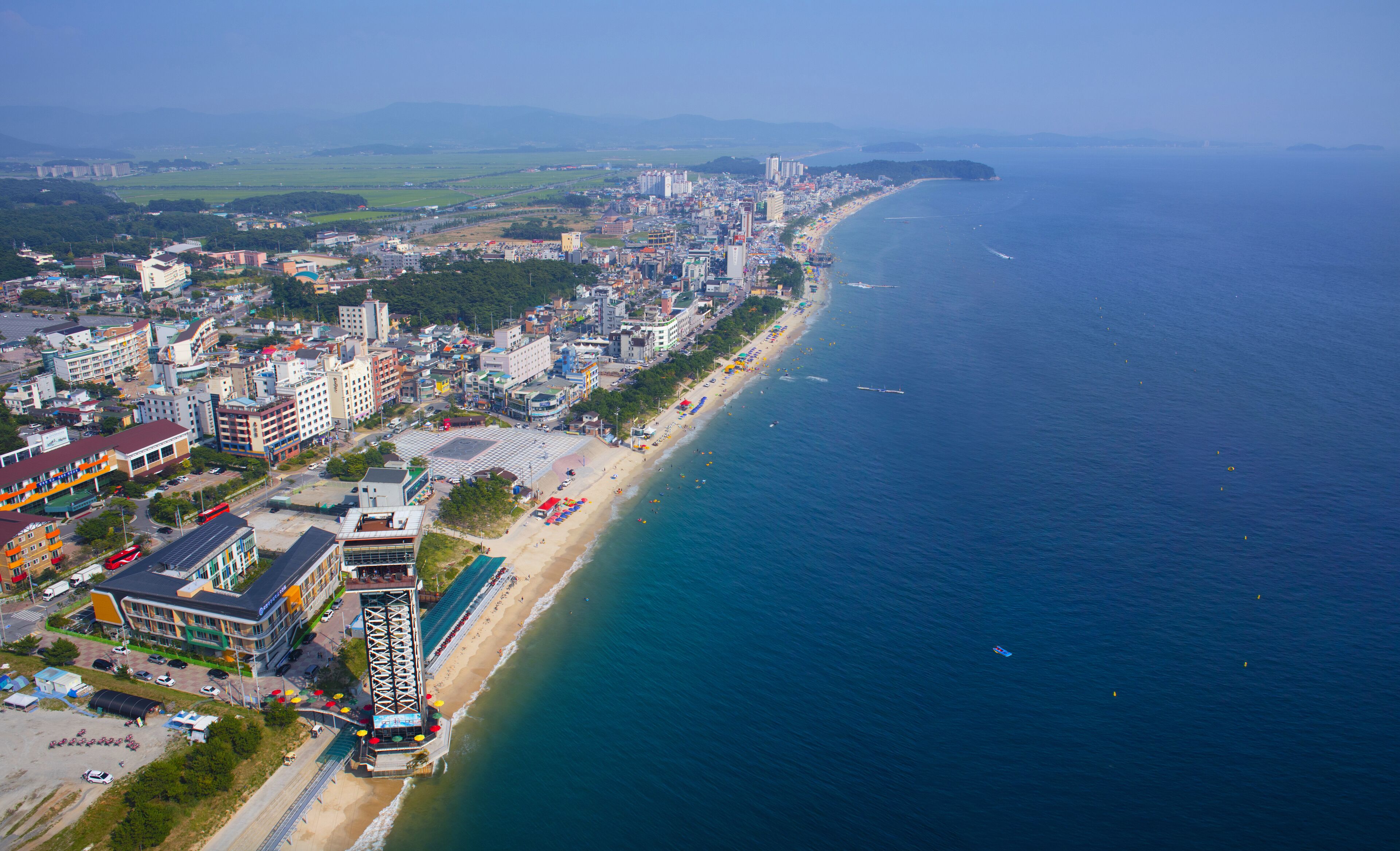 An aerial view of a coastal city with a beach, buildings, and a clear sky.