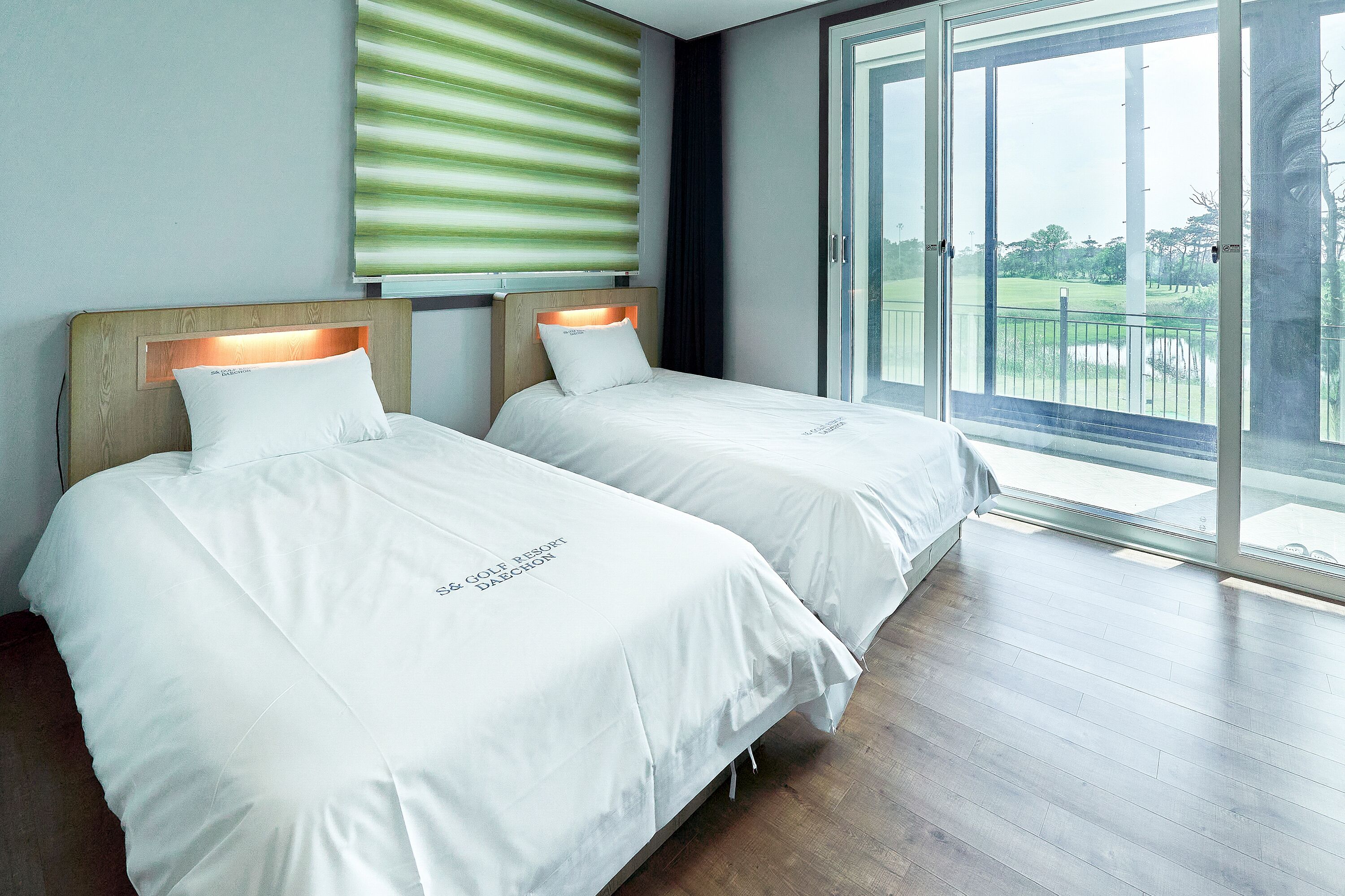 A hotel room with two beds, a large window with a view of a golf course, and a sliding glass door to the outside.