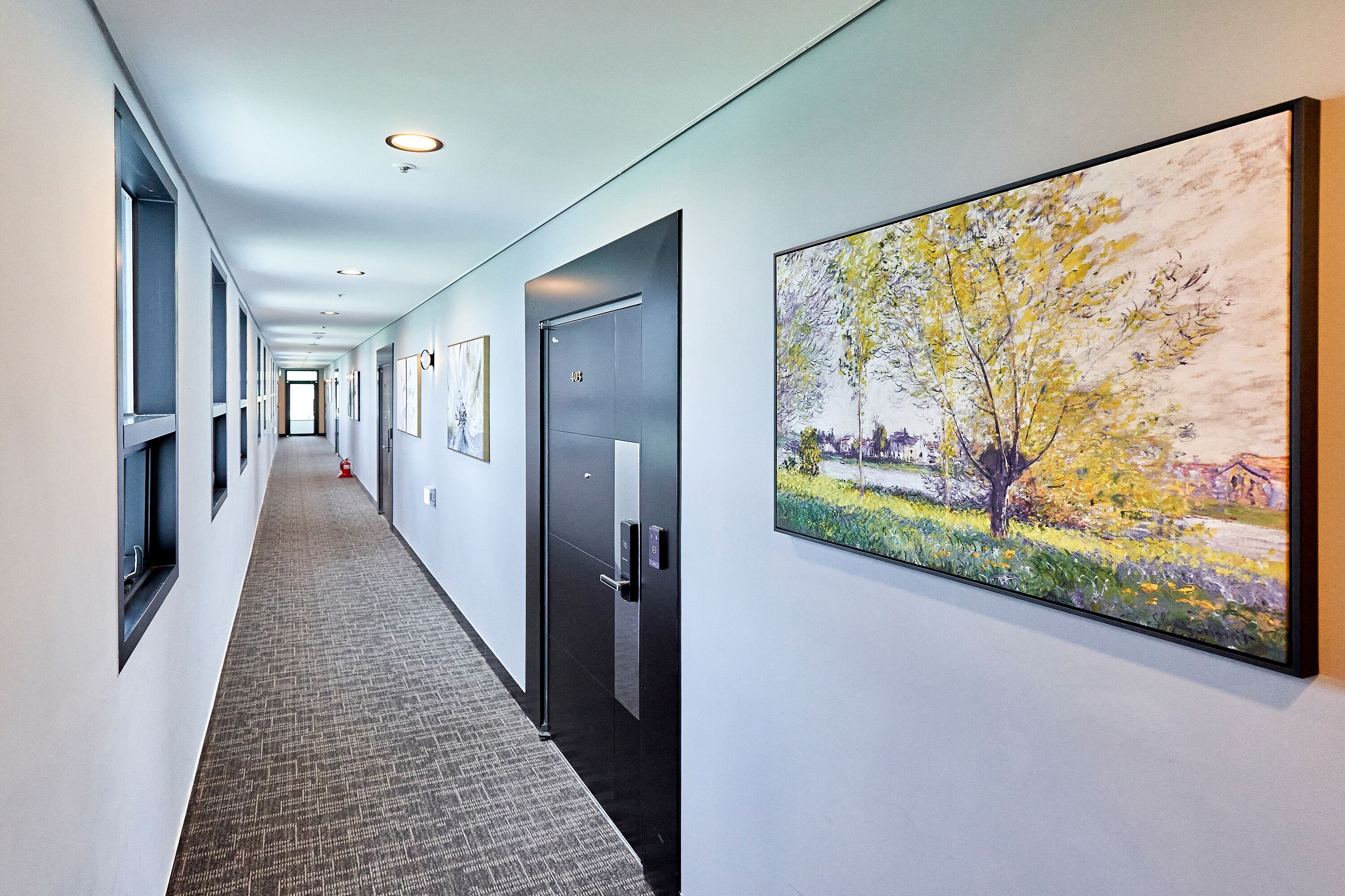 A long, narrow hallway with doors on one side and a large painting on the wall.