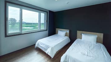 A hotel room with two beds, a large window with a view of a green landscape, and a ceiling light.