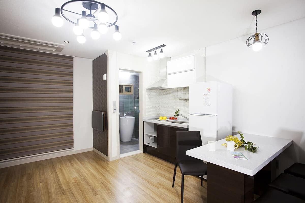 Una cocina compacta con refrigerador, lavamanos y una zona de comedor con mesa y sillas.