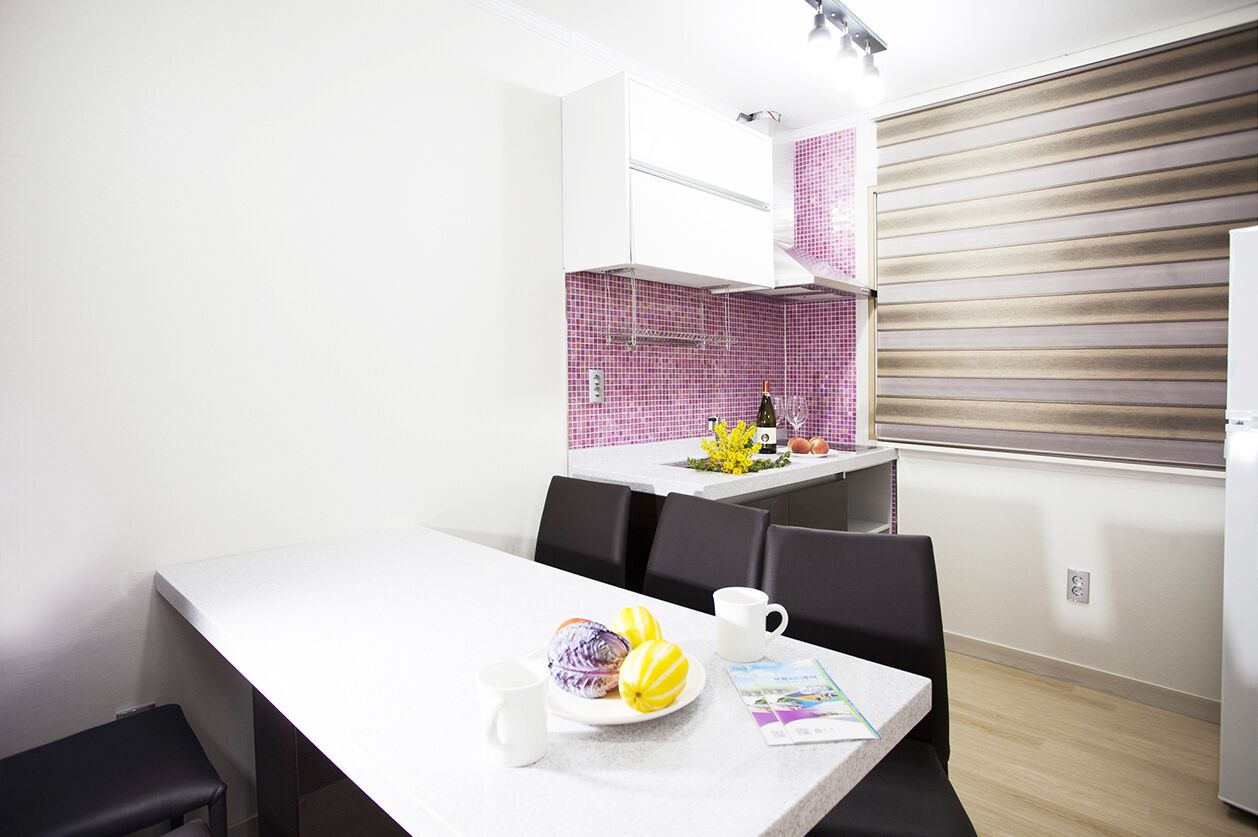 A modern kitchen with white cabinets, a pink tiled backsplash, and a dining area with a white table and chairs.