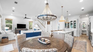 A spacious living room with a large round wooden table, wicker chairs, a chandelier, and a television. - 30A ☀️ 6 Seat Golf Cart | *Heated & Chilled Pool | Gated | Beach Equip ☀️Near Restaurants (Santa Rosa Beach)