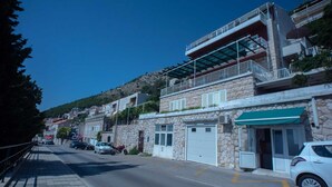 Una calle con edificios de piedra, un coche blanco estacionado al lado y un cielo azul despejado.