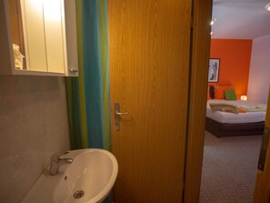 A bathroom with a sink and a wooden door leading to a bedroom with a bed and a nightstand. - Apartment Cantabile II (Dubrovnik)