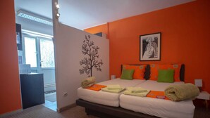Una cama doble con almohadas anaranjadas y verdes, un cuadro enmarcado en la pared y una ventana con vistas al exterior.