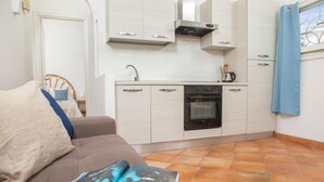 Um espaço compacto com cozinha compacta, um sofá com uma revista e vista para o exterior através de uma janela.
