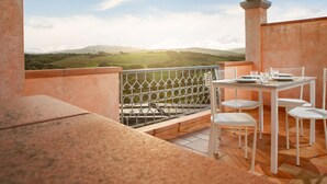 Um terraço com mesa e cadeiras, vista para colinas verdes e guarda-corpo de metal.