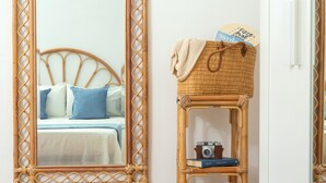 Um quarto com uma cama, um espelho, uma cesta de vime numa prateleira e uma câmera.
