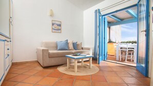 Un soggiorno con divano, un tavolino e vista su un patio esterno da una porta aperta.