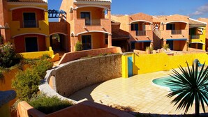 Une rangée de bâtiments colorés de style méditerranéen, dotés de balcons, d’une piscine et d’un mur en pierre.