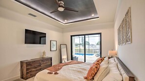 A bedroom with a bed, a ceiling fan, a TV, a window with a view of a pool, and a nightstand with a lamp. - Private Pool: Canalfront Home in Cape Coral (Cape Coral)
