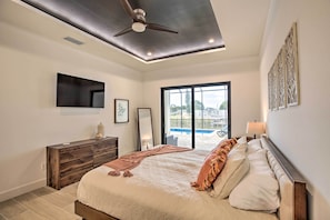 A bedroom with a bed, a ceiling fan, a TV, a window with a view of a pool, and a nightstand with a lamp. - Private Pool: Canalfront Home in Cape Coral (Cape Coral)
