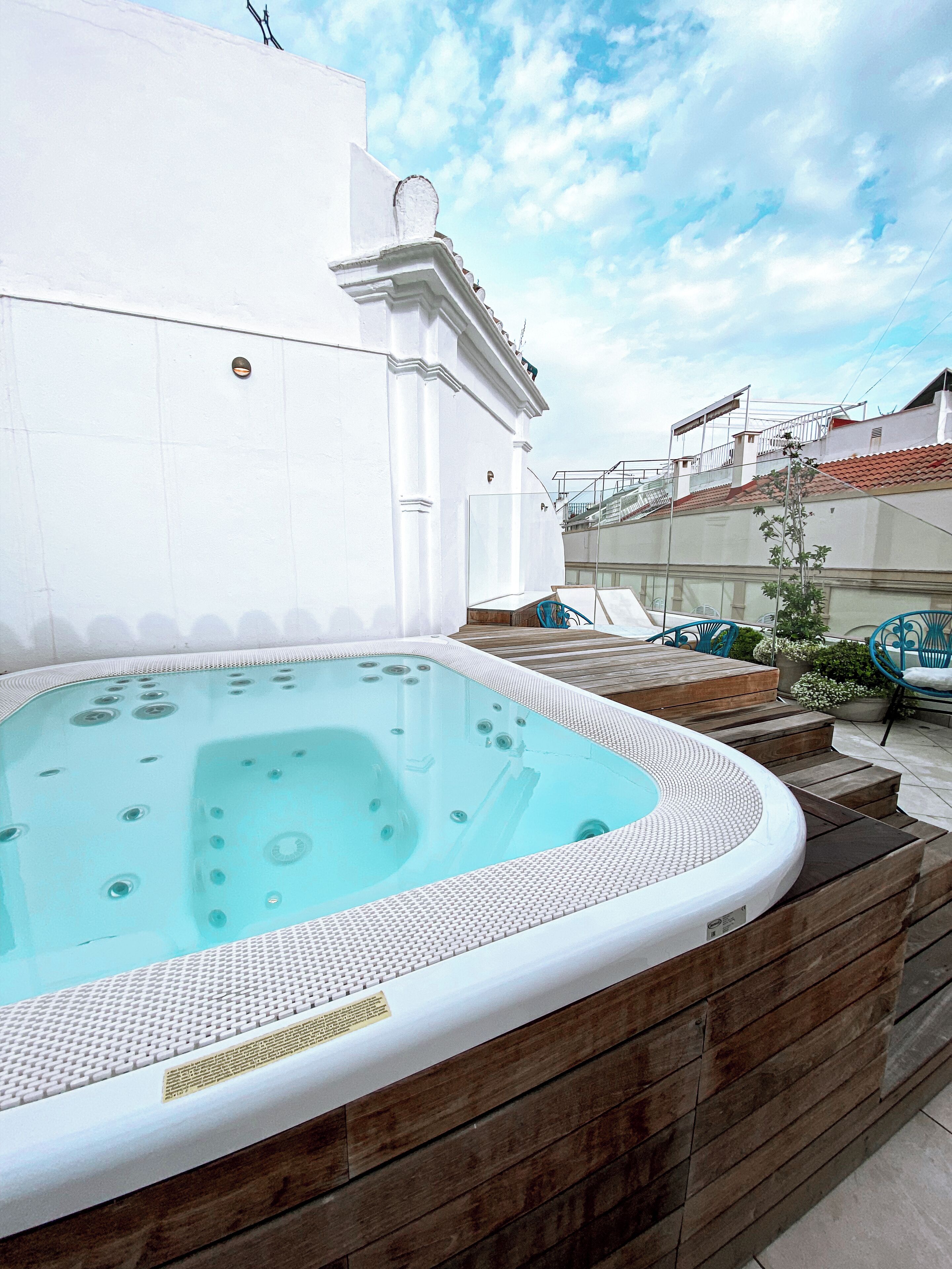 Un bain à remous doté d’une terrasse en bois et d’escaliers, entouré d’un mur blanc et surplombant un ciel dégagé.