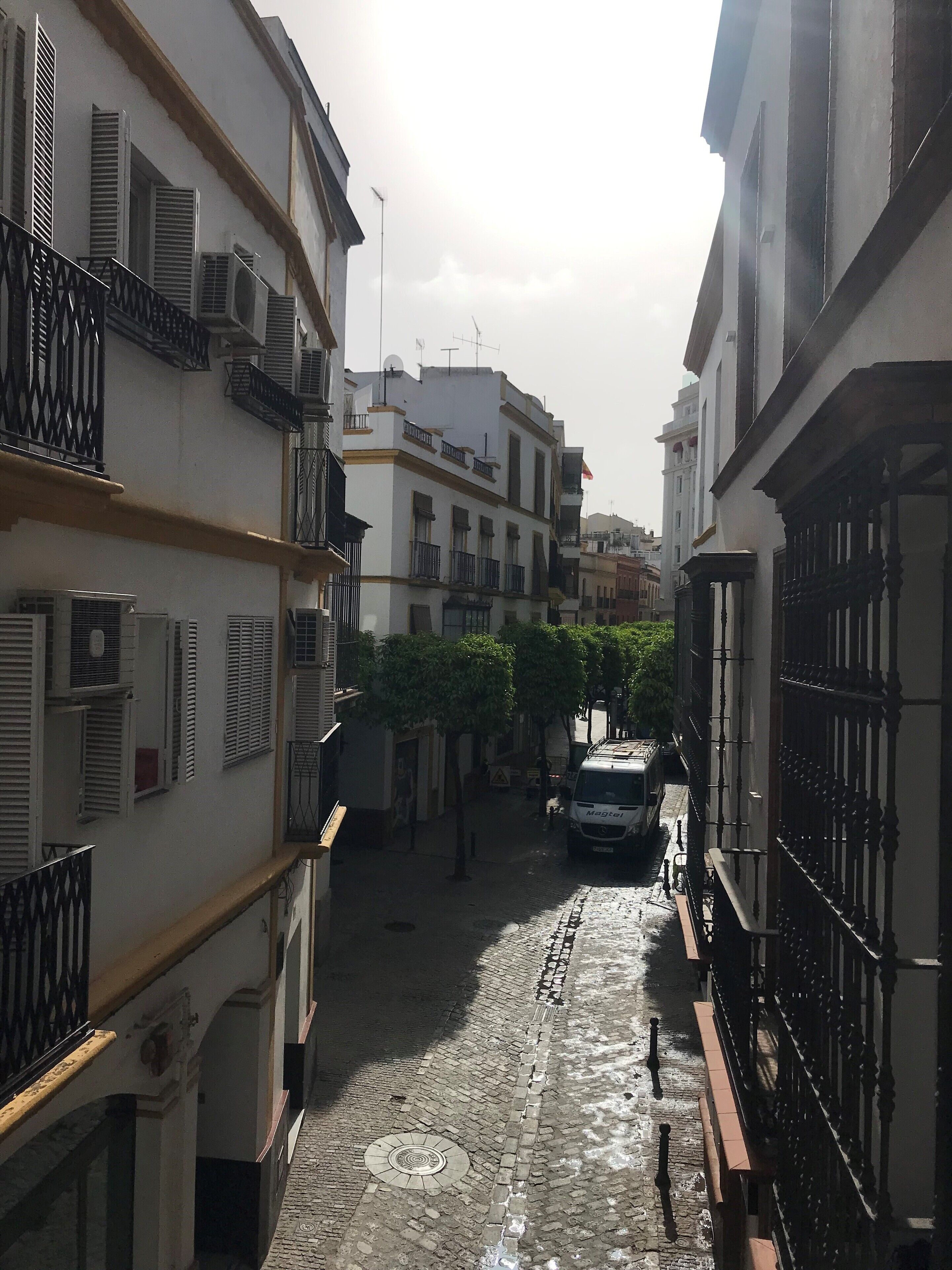 A narrow cobblestone street flanked by buildings with balconies and air conditioning units.