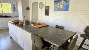 A modern kitchen with a large island, white cabinetry, and a painting of boats on the wall. - Very attractive holiday home with pool, wonderful terrace and garden (Le Canon)