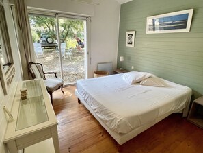 A bedroom with a bed, a chair, a table, and a view of the outdoors.