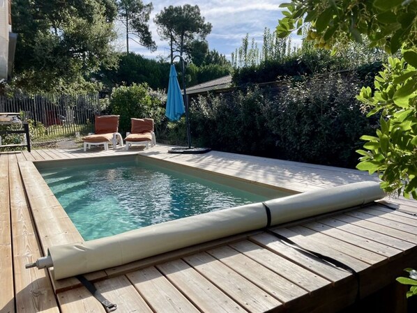 A rectangular swimming pool with a wooden deck and two lounge chairs.