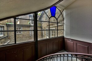 A corner of a building with a stained glass window, stone walls, and a wooden staircase.