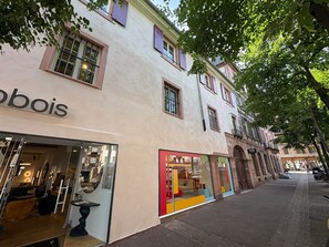 A street with storefronts, including a furniture store with a glass facade and another with colorful interior displays.