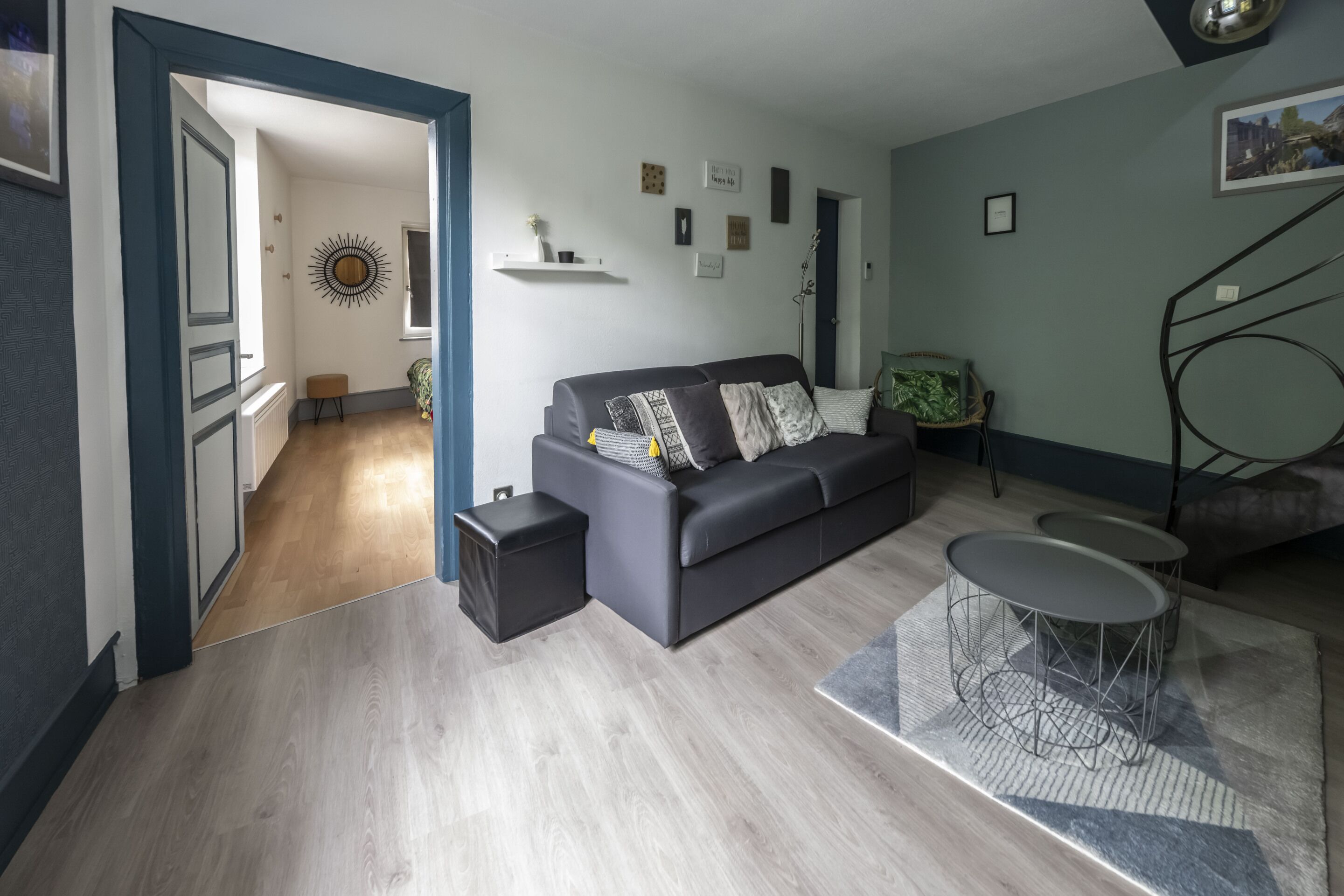 Een moderne woonkamer met een grijze bank, een salontafel en een bijzettafeltje. Een trap leidt naar een hoger gelegen verdieping.
