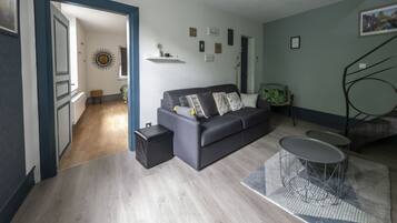Een moderne woonkamer met een grijze bank, een salontafel en een bijzettafeltje. Een trap leidt naar een hoger gelegen verdieping.