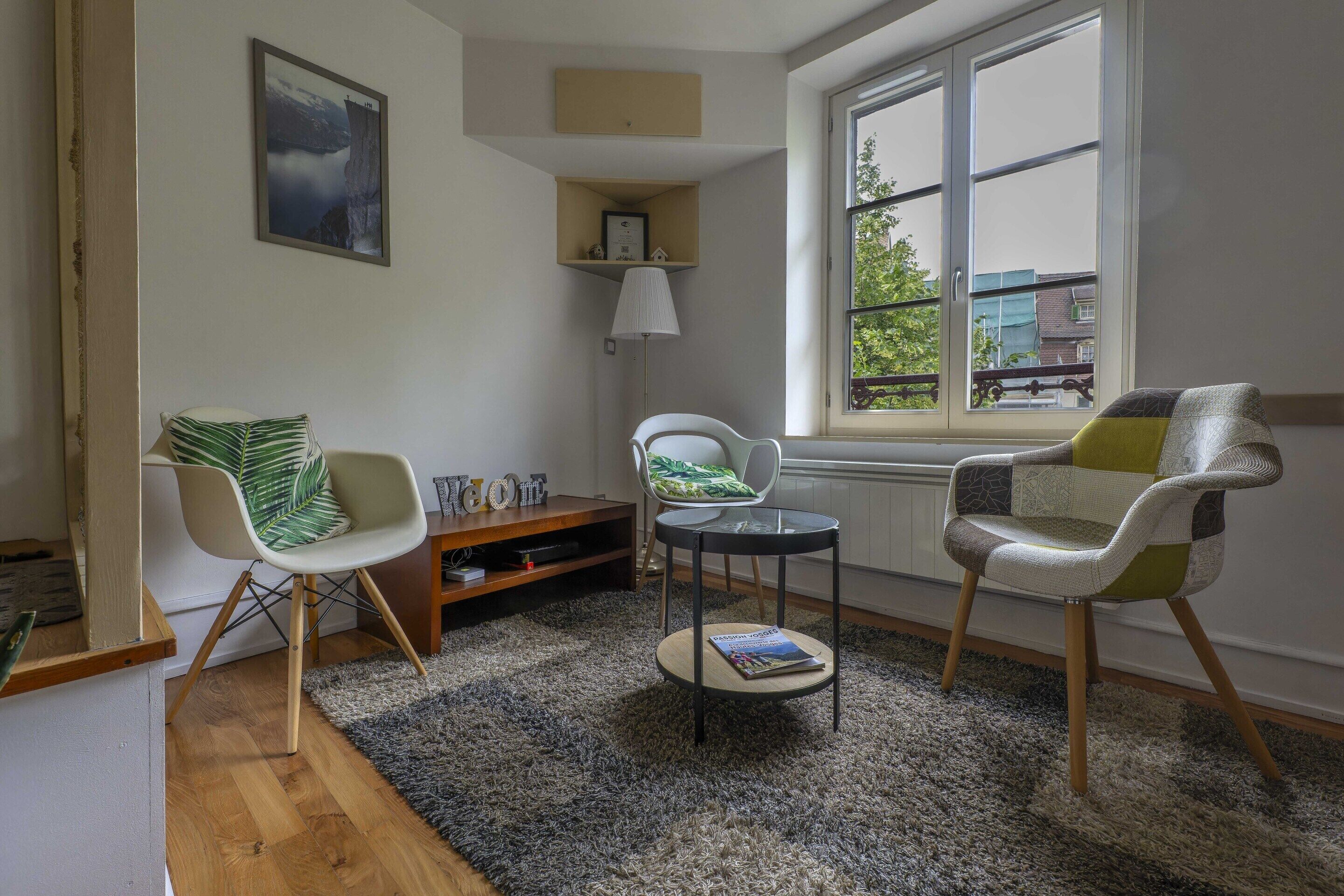 A living room with a large window, two chairs, a small table, and a bookshelf.