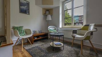 A living room with a large window, two chairs, a small table, and a bookshelf.