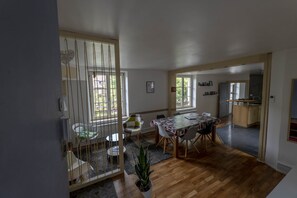 A spacious dining area with a wooden table and chairs, a potted plant, and a view of the kitchen through an open doorway.