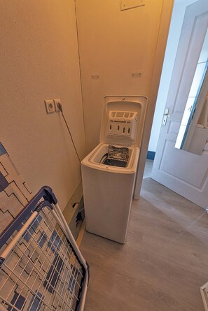 A compact laundry room with a washing machine and a dryer, a power outlet, and a door leading to another room.