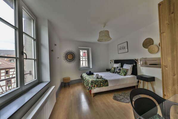 A bedroom with a large window, a bed with a floral bedspread, a round wall decoration, and a 'Home' sign on the wall.