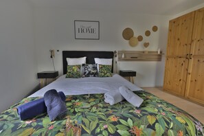 A bedroom with a bed, a wooden wardrobe, a bedside table, a wall-mounted shelf, and a wall decoration.
