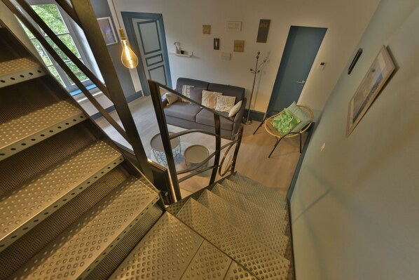 A staircase with a metal handrail leading to a living area with a sofa, a lamp, and a wall with framed pictures.