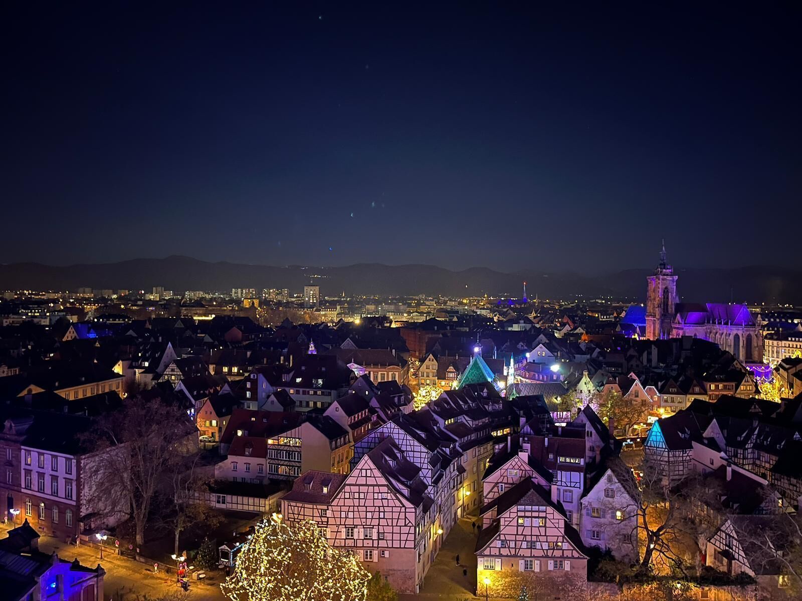 Una vista notturna di una città con edifici illuminati e una torre campanaria in evidenza.