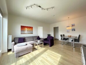 Un salon moderne avec un canapé gris, une table basse, un fauteuil violet et un coin repas comprenant une table et des chaises.