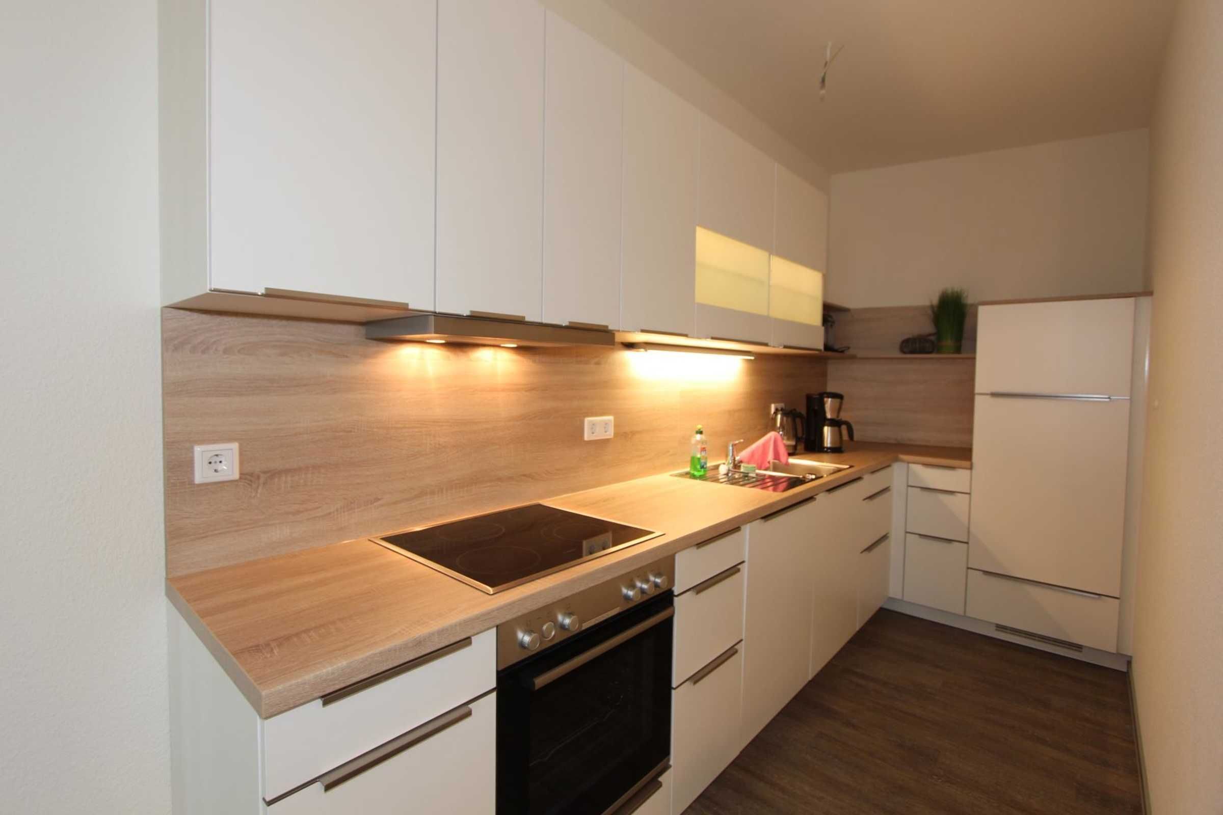Una cocina moderna con encimera de madera, horno empotrado y muebles blancos.