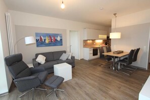 A modern living room with a grey sofa, a white ottoman, and a dining area with a table and chairs.