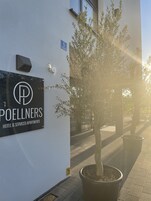 Señalización para 'POELLNERS HOTEL & SERVICED APARTMENTS' con un árbol en maceta al frente.