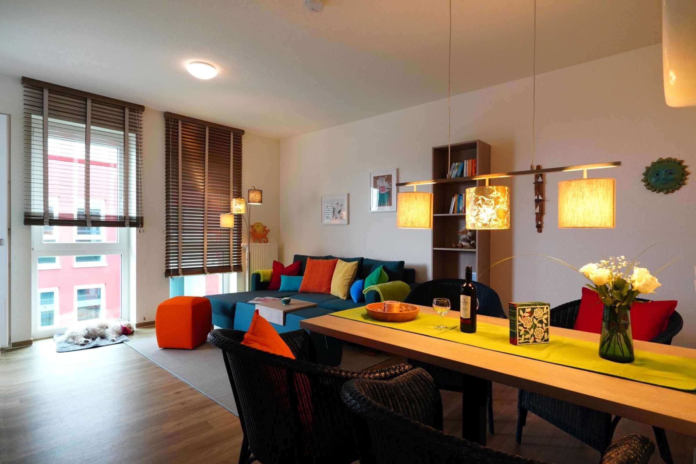 A modern living room with a sofa, chairs, a dining table, and a bookshelf.