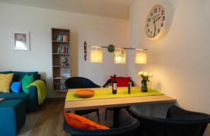 Un salon confortable avec un canapé, une table à manger et des chaises, une bibliothèque et une horloge murale.